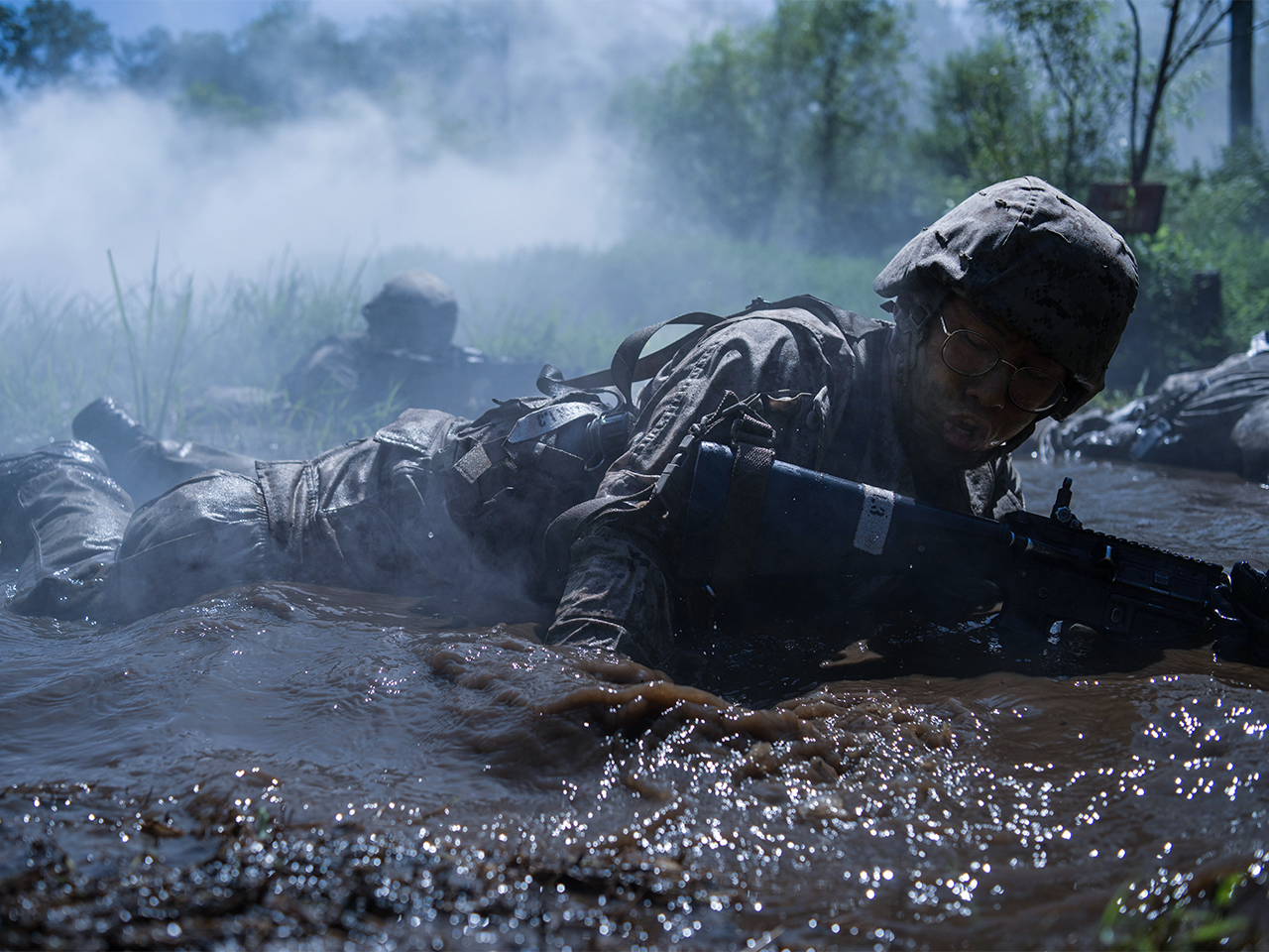 Marine in full combat gear and helmet crawling through muddy water during tactical training exercise.