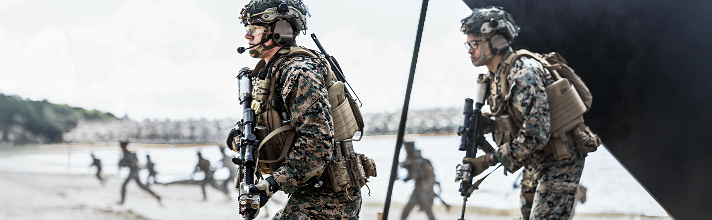 Marine officers in full combat gear with communications equipment lead amphibious training operation at Camp Schwab beach.