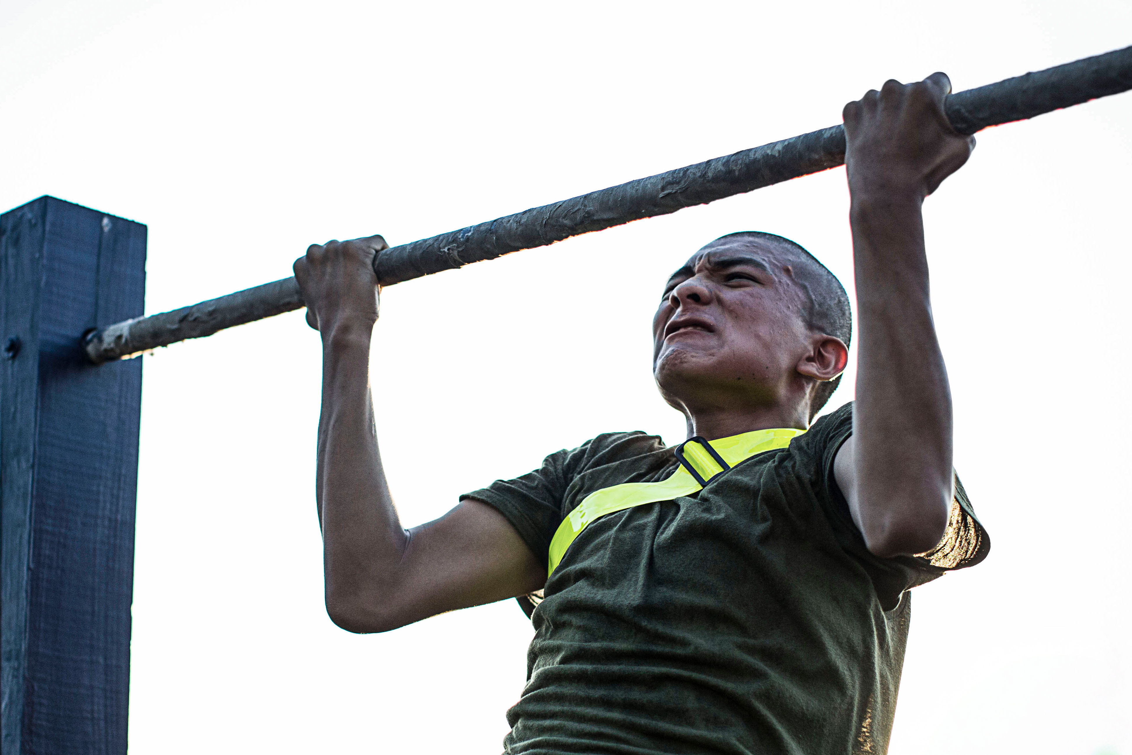 Marine Recruits completes a pull-up during Initial Strength Test, wearing reflective belts as part of physical fitness evaluation.