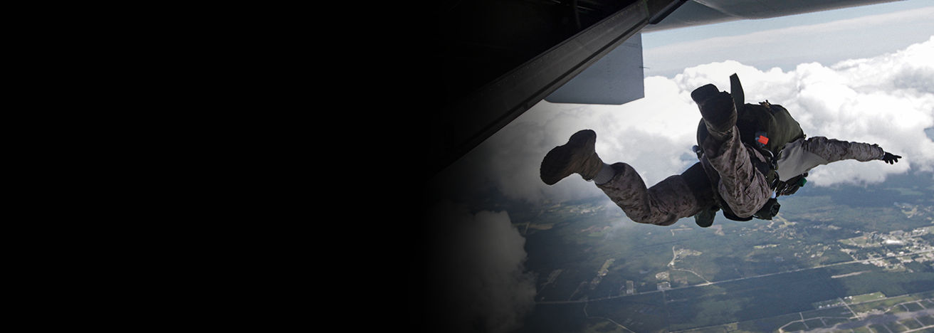 Marine paratrooper jumping from aircraft during airborne operations training exercise over terrain below.