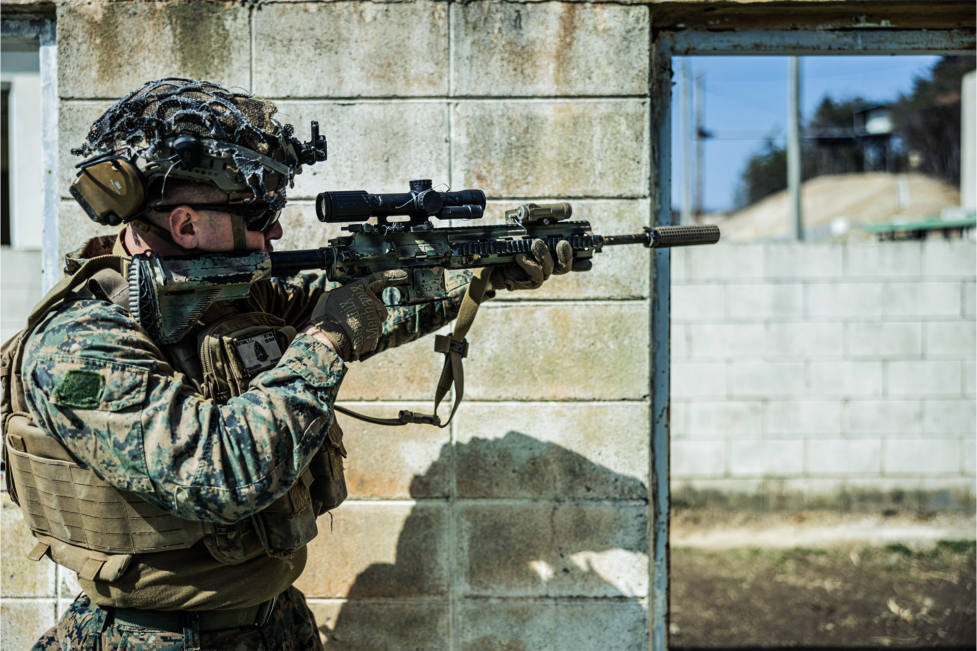 Marine aims M4 carbine with scope and suppressor through window during urban warfare training in South Korea.