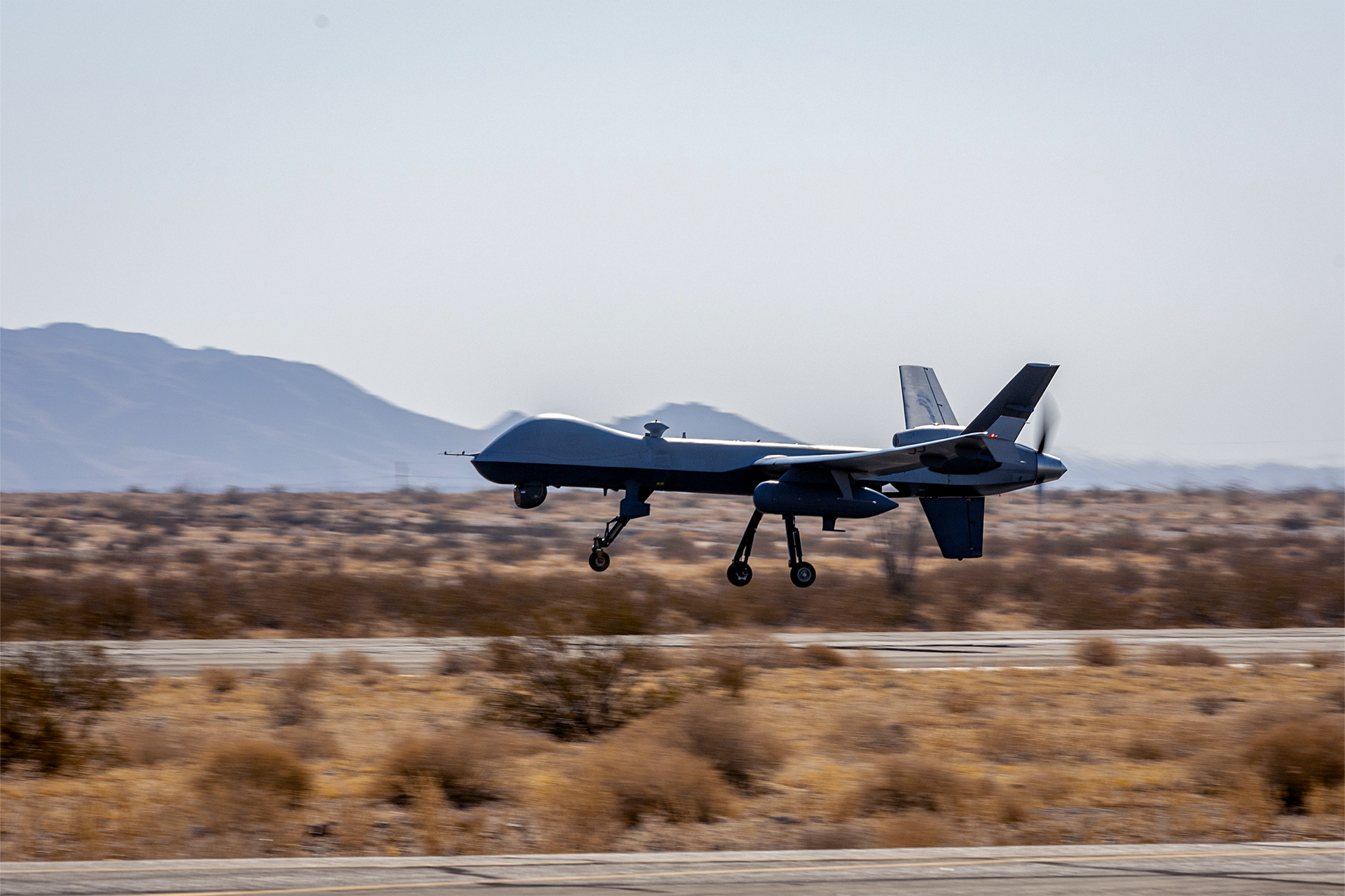 MQ-9 Reaper unmanned aerial vehicle takes off from desert airfield with mountains in background during operations.