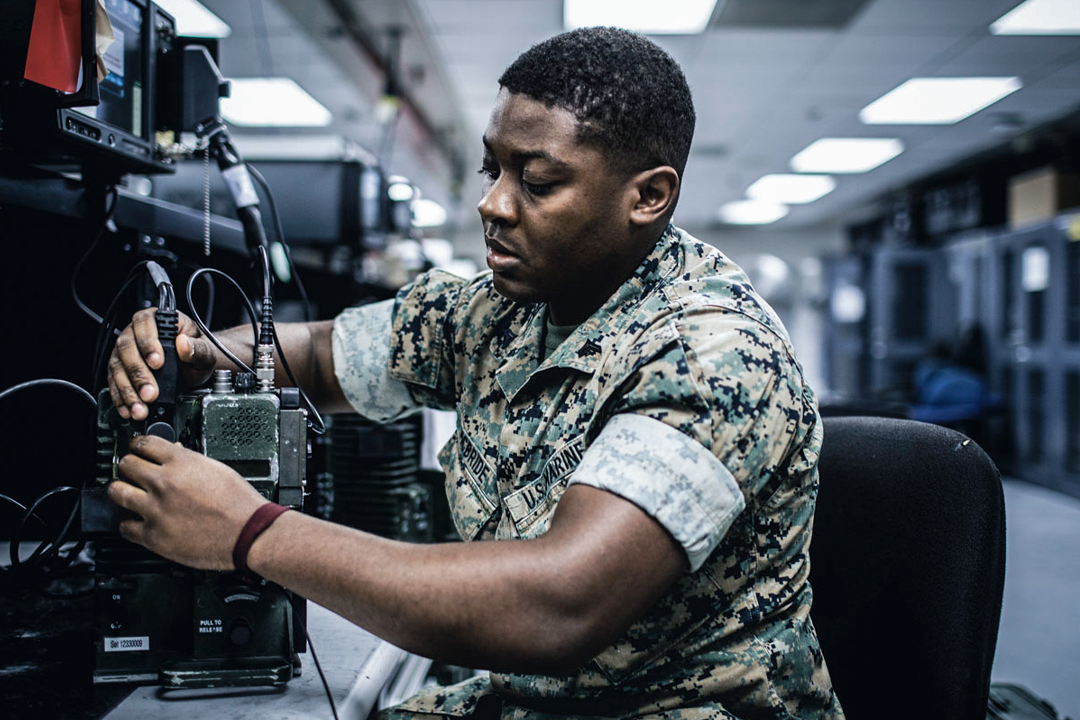 A electronics maintenance Marine works on a piece of communications equipment in a workshop.
