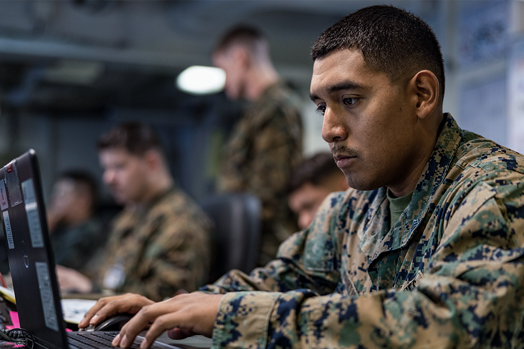 An Administrative and Data Specialist Marine works at a computer in a command center alongside other Marines. 