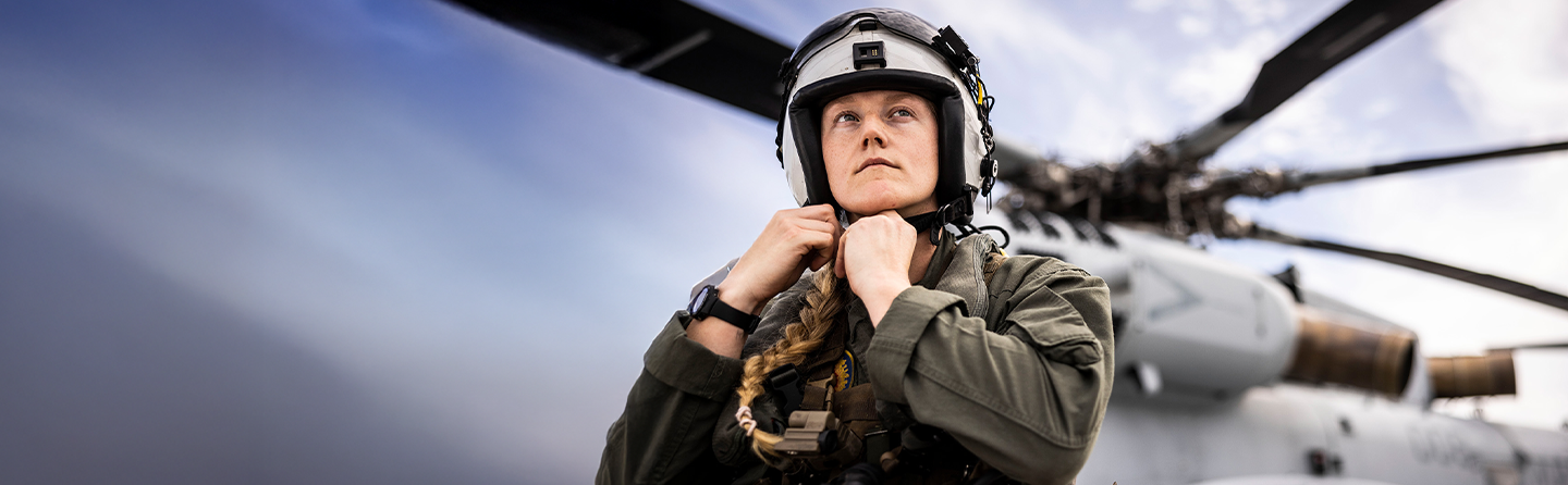 Captain Kricket Harper adjusts flight helmet on flight line with helicopter in background at Camp Lejeune.