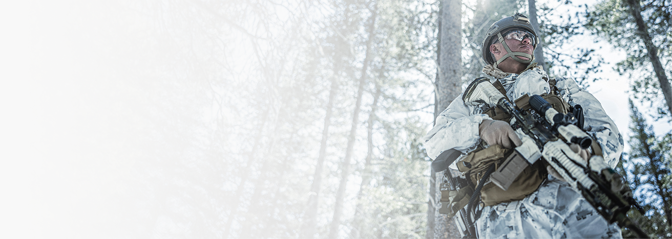 A Marine in snow camouflage and helmet holds rifle during cold weather training at Mountain Warfare Training Center Bridgeport.